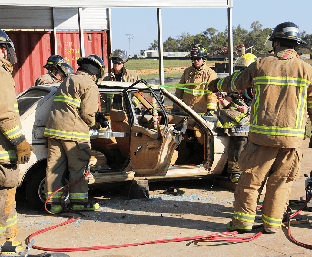 Firefighters handle mock car crash, removing doors and mock passengers.